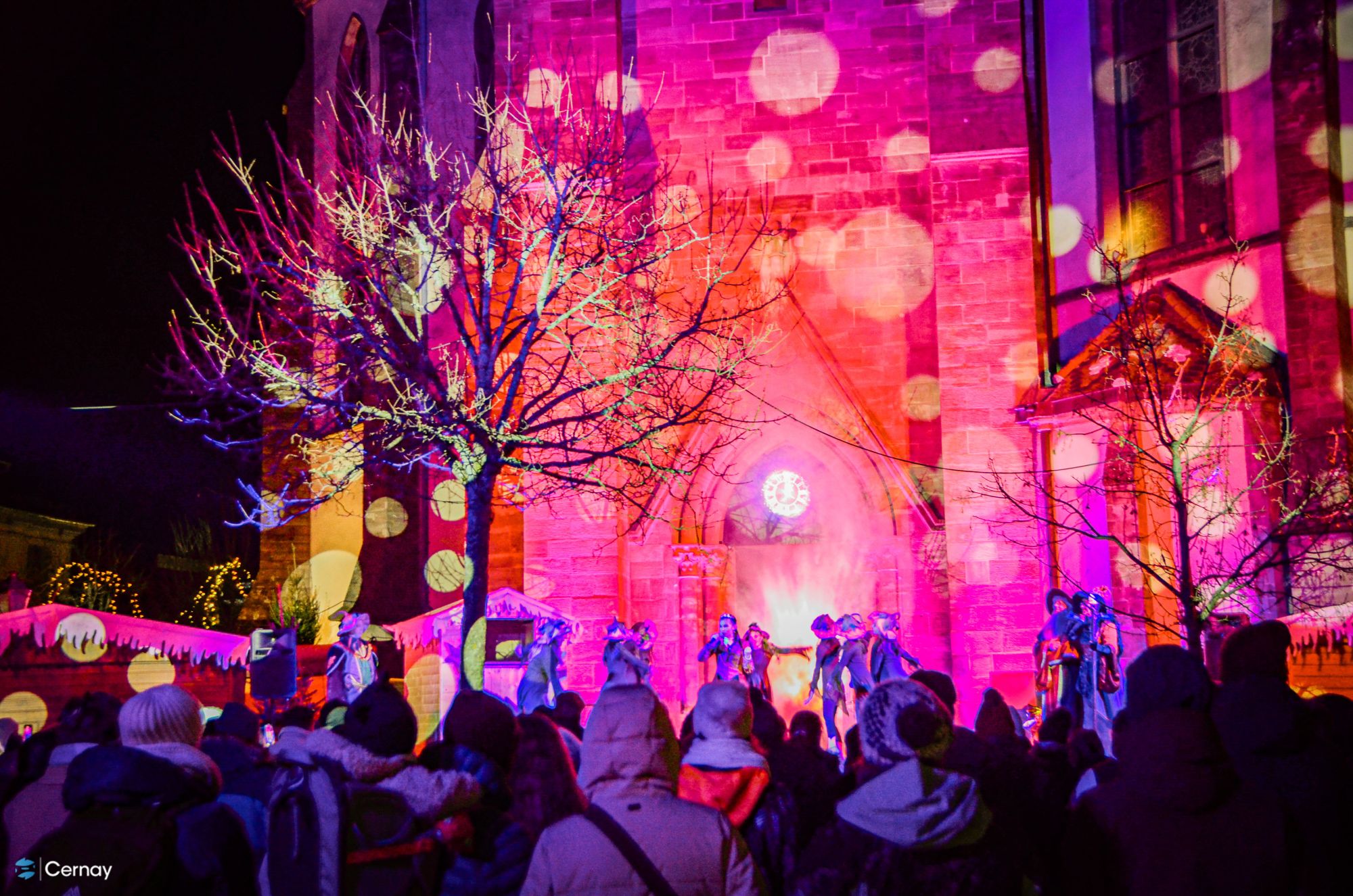 L'Horloge magique du Père Noël à Cernay les 12,13,14,19,20 et 21/12/25 On y voit une scène avec des personnages de Noël devant le clocher de l'église de Cernay